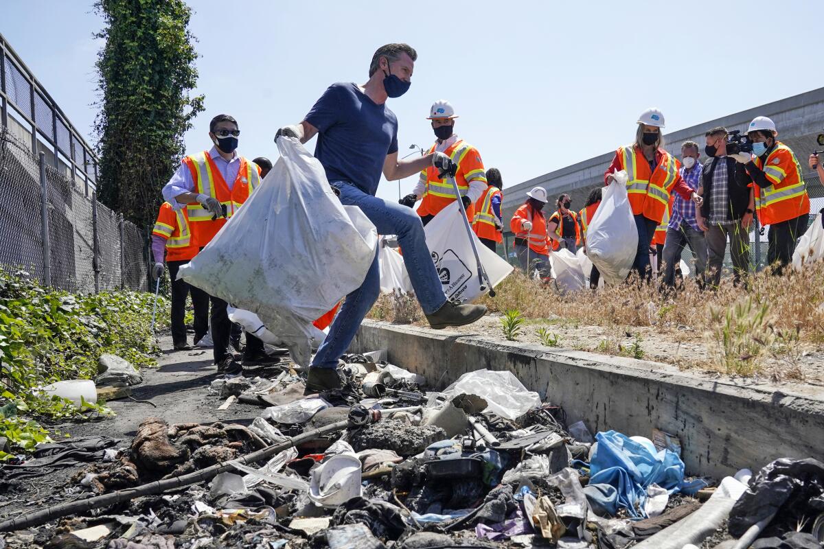 Gov. Gavin Newsom carries a bag of trash. 