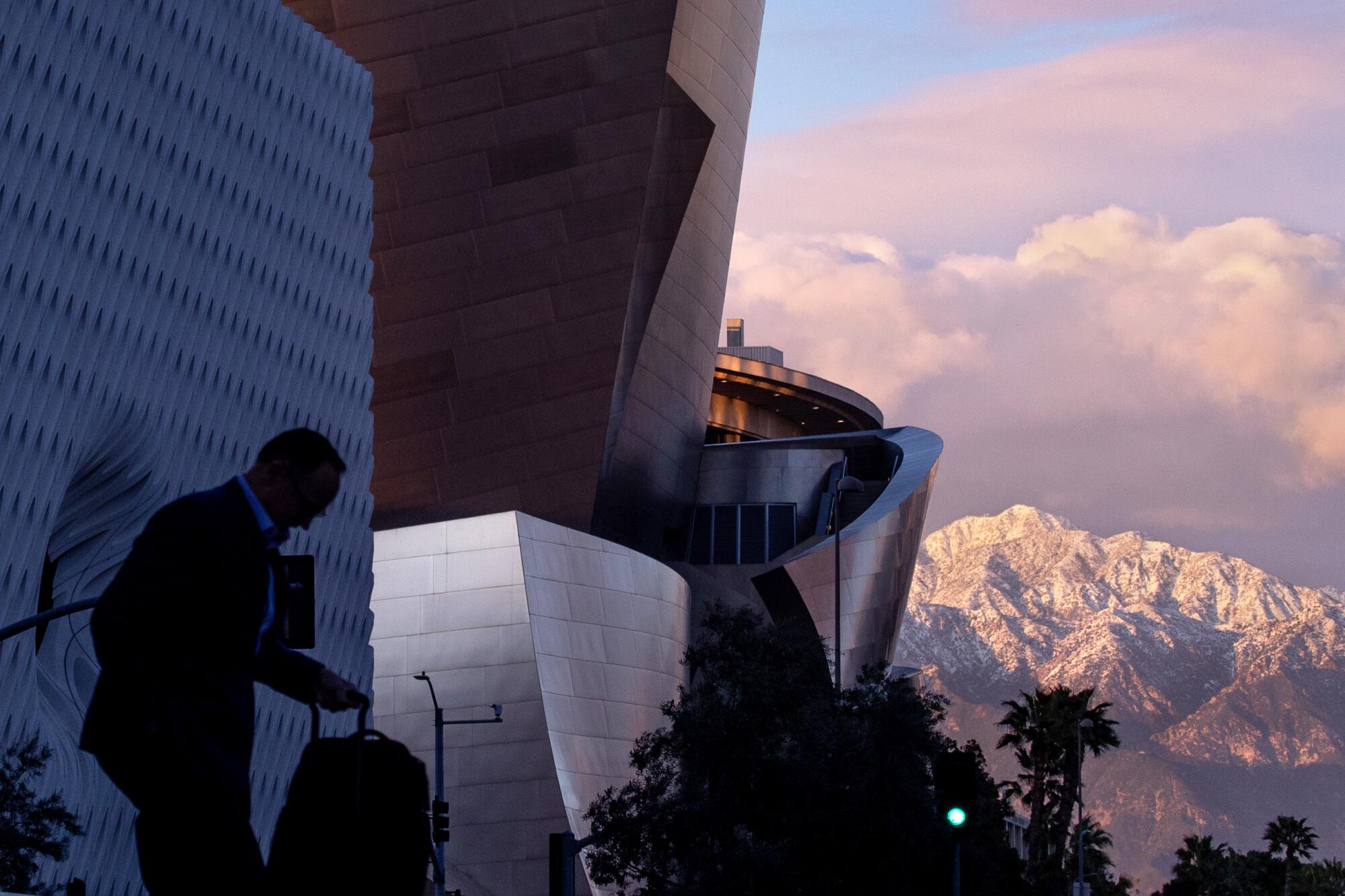 A silhouette of a man in front of Disney Hall, with snow-topped mountains in the background