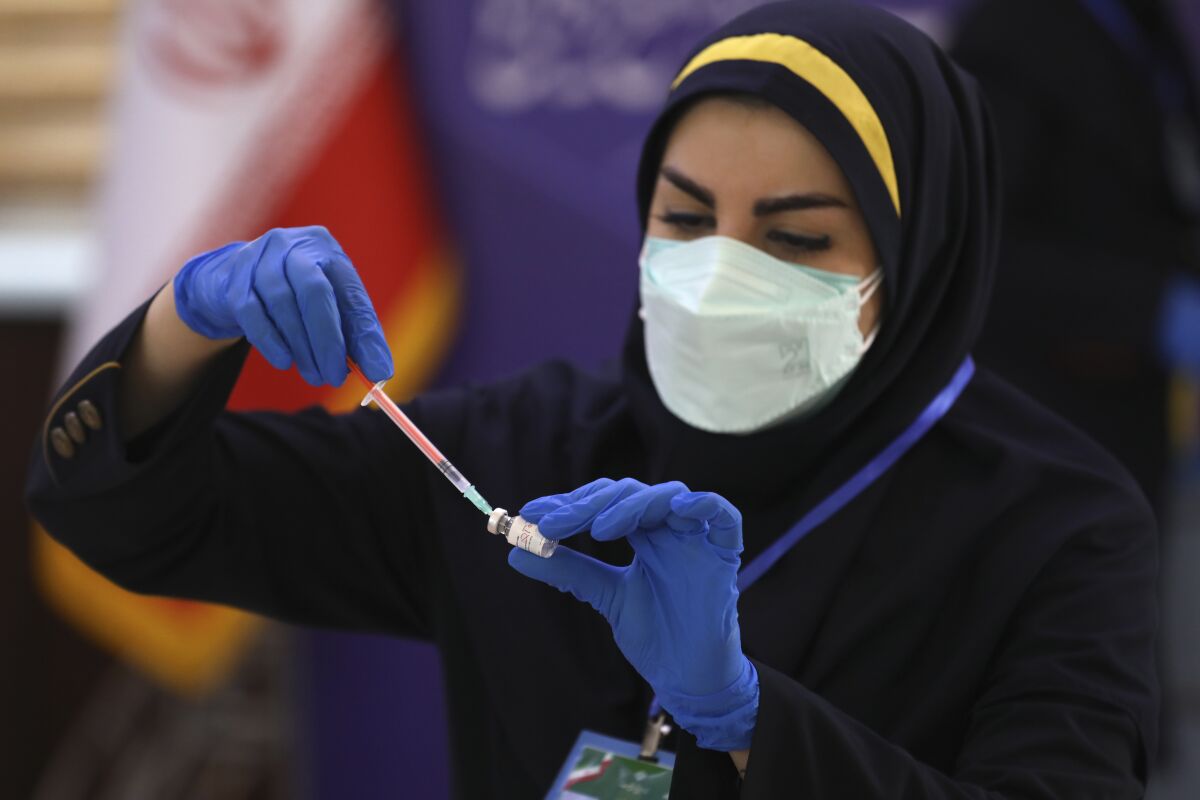 A female medic in headscarf and mask draws a dose of vaccine