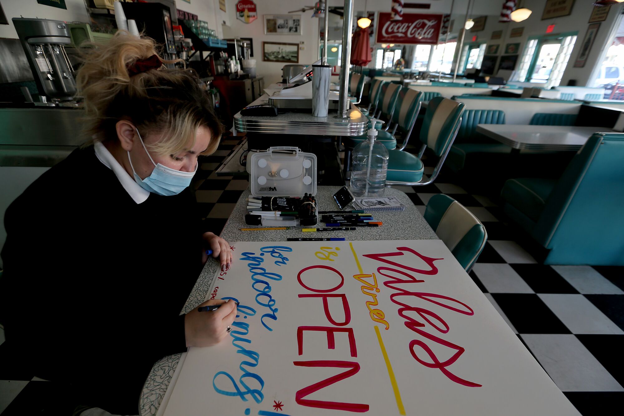 A masked woman writes on a sign that reads Dales Diner is Open for indoor dining