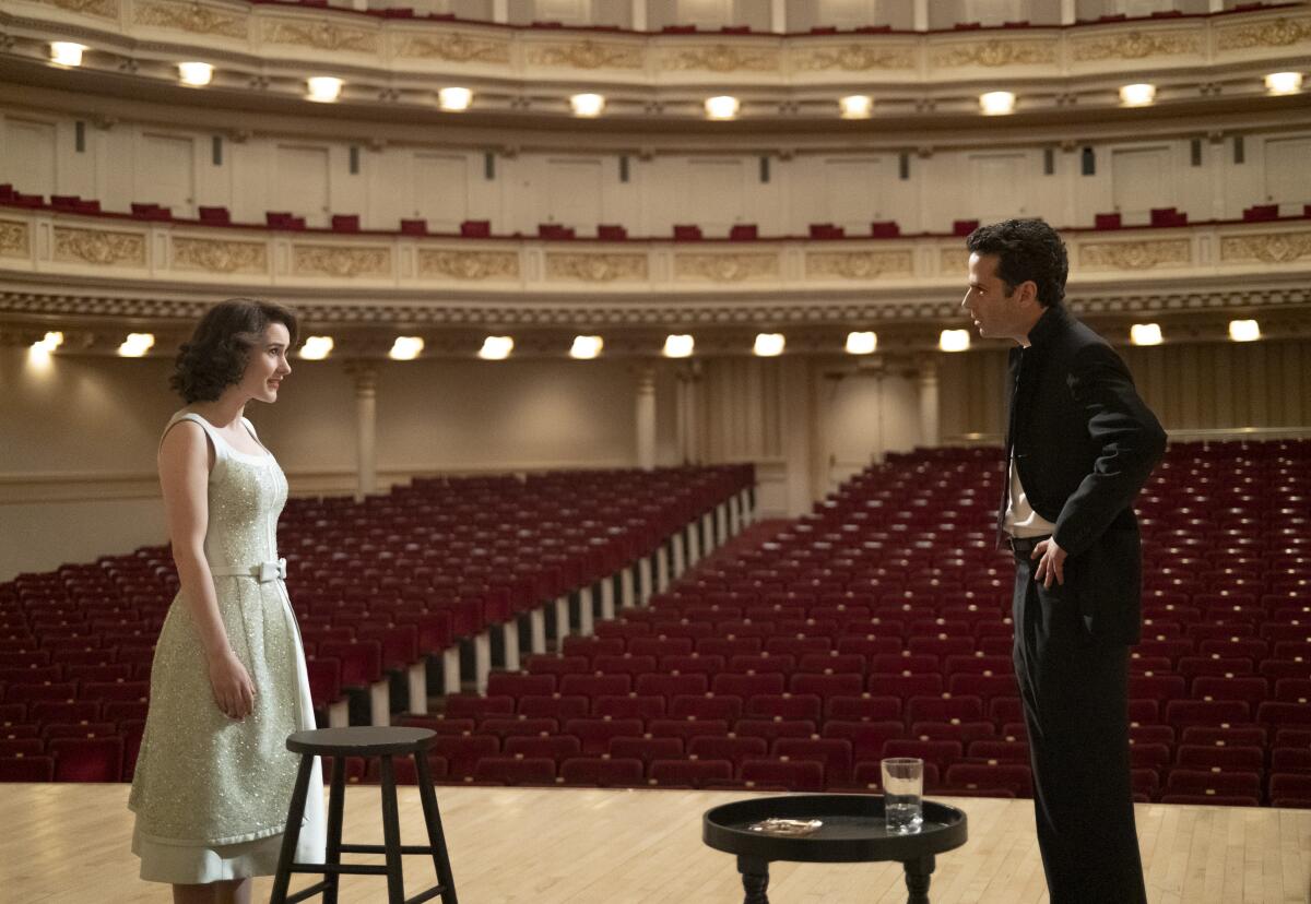 A man and a woman stand on the stage of an empty theater.