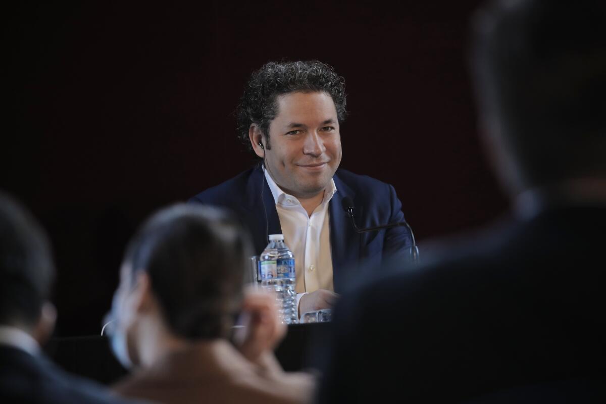 Gustavo Dudamel in a black jacket and white shirt looking toward a group of people