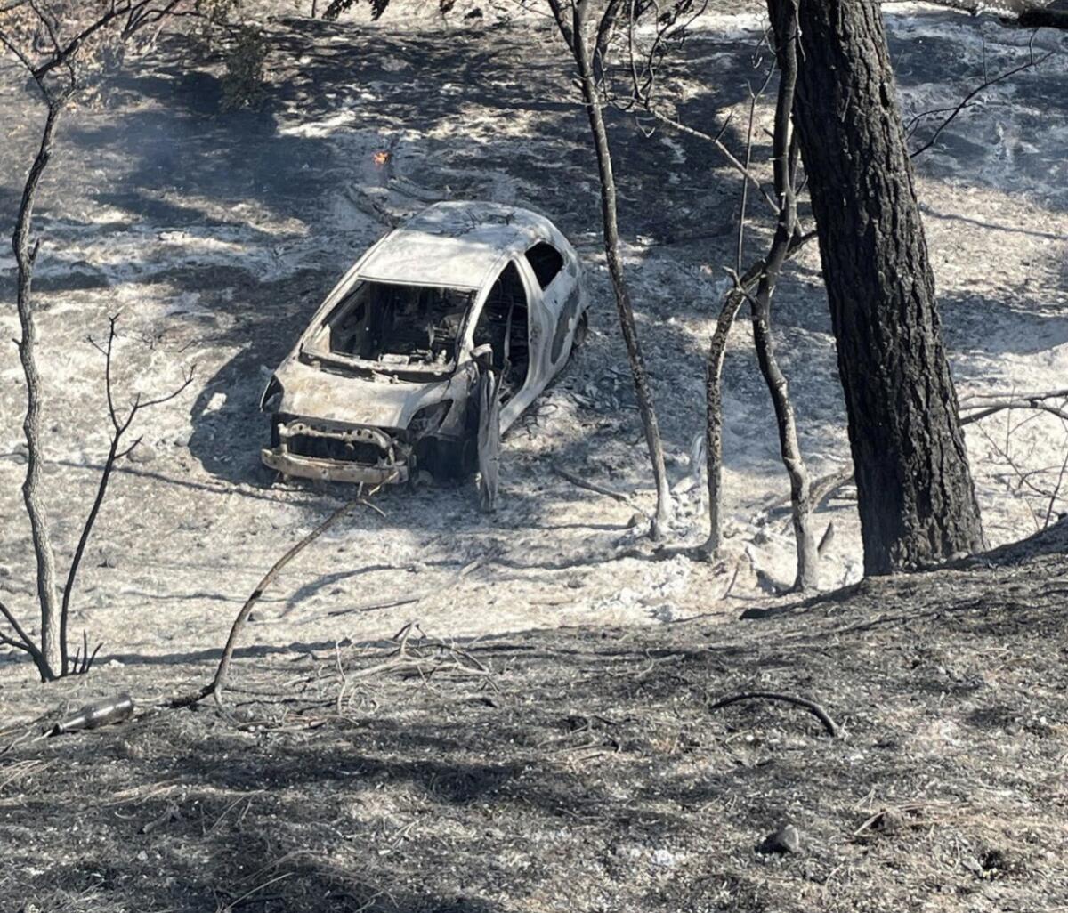 A burnt car at the bottom of a fire-scorched gully