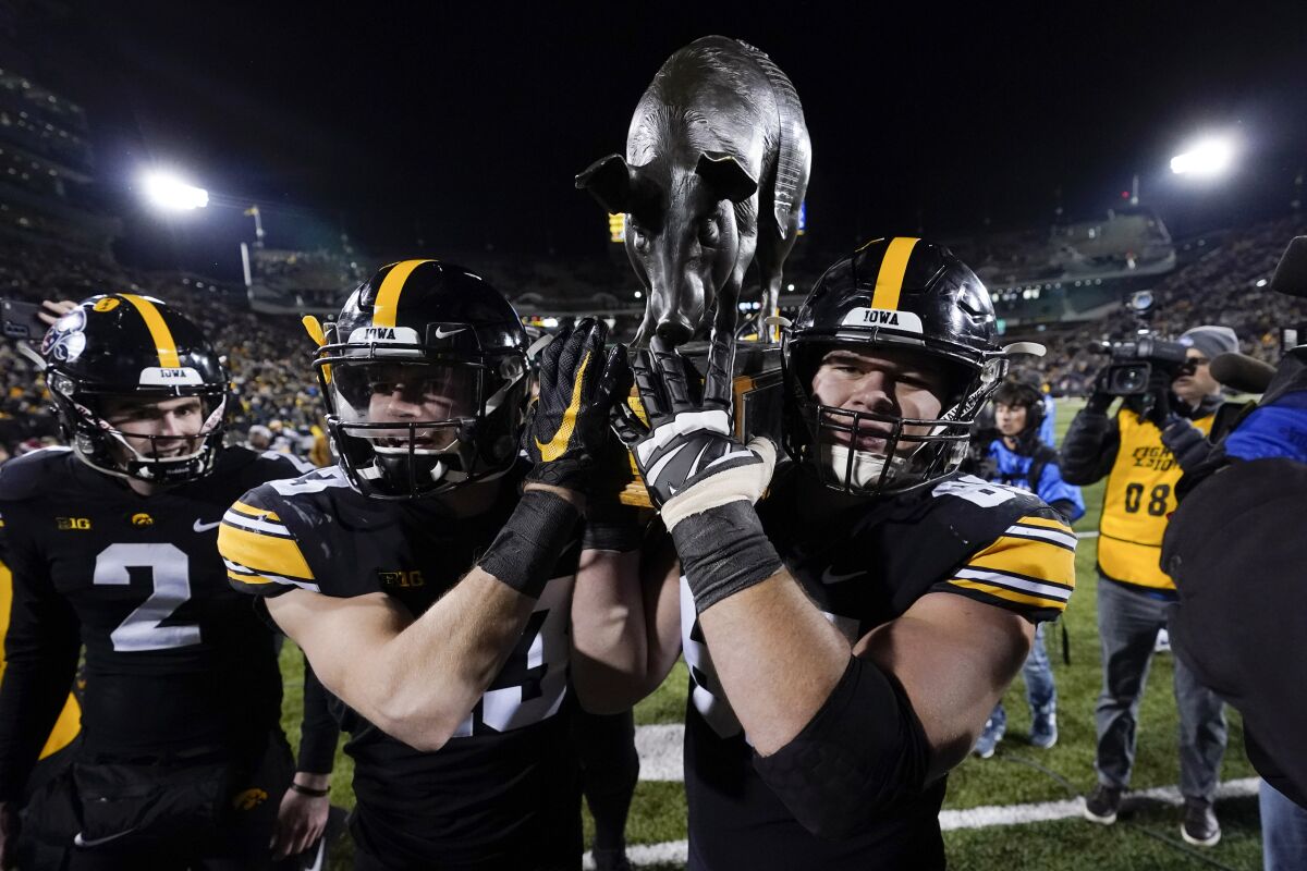 Iowa offensive lineman Tyler Linderbaum, right, helps carry the Floyd of Rosedale trophy off the field Nov. 13, 2021.