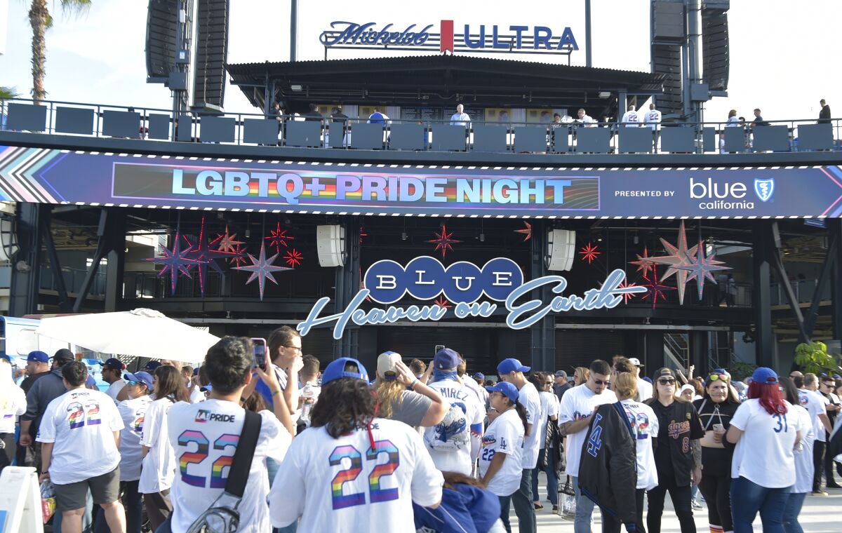 People dressed in Dodgers and Pride colors enter the entrance of a baseball stadium.