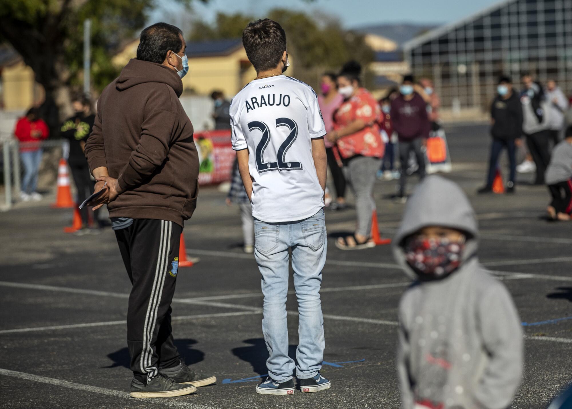 Lazaro Velazquez, 55, left, and his son Enrigue, 14, wait in line with others at Lompoc High School.