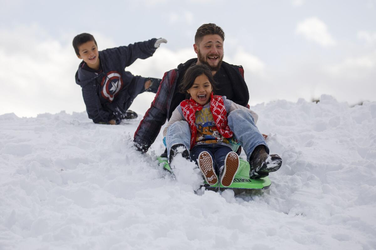 A man and two children ride sleds down a snowy hill in Lebec, Calif.