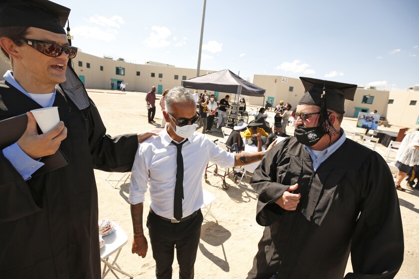 A professor talks with two men in caps and gowns in the prison yard. 