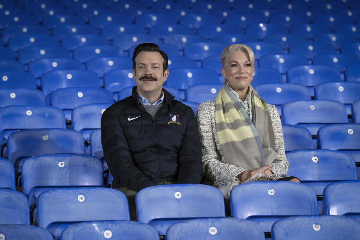 A man and woman sit next to each other in an empty stadium with blue seats.