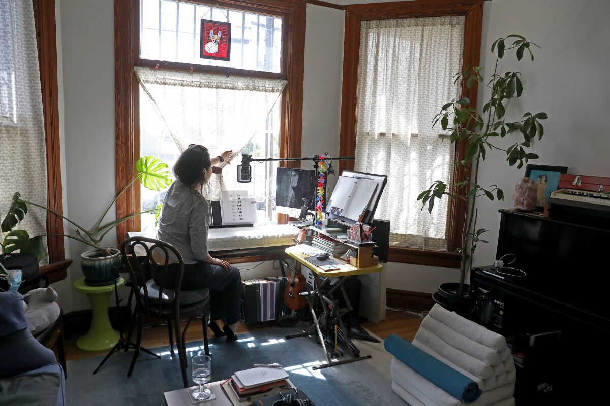 A person sits with their back to camera, adjusting a window curtain while sun is entering the room