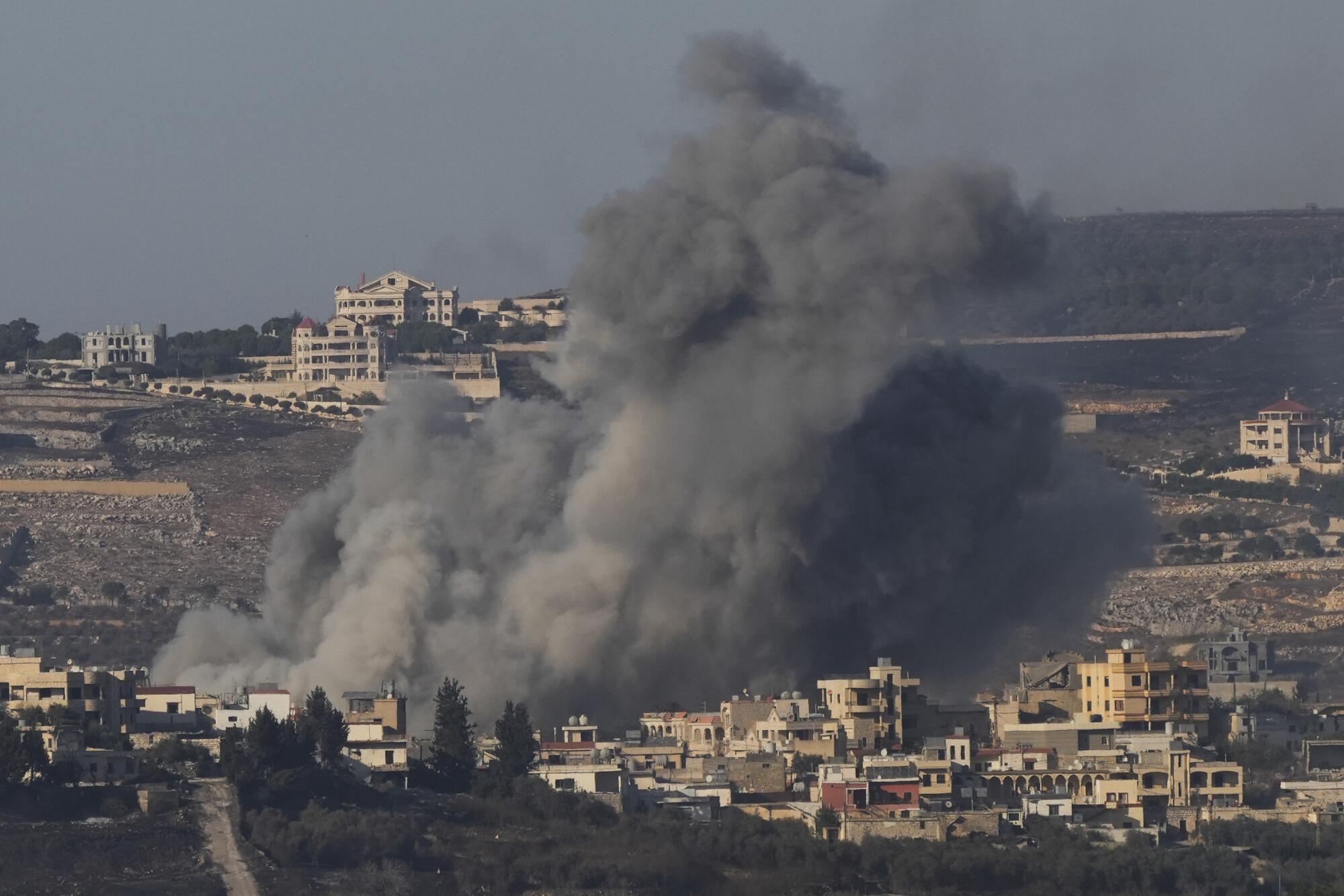 Huge clouds of gray smoke rise over a landscape of buildings