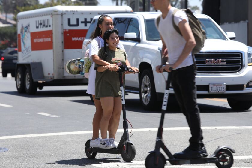 Girls ride across Pacific Avenue on a single Bird scooter as another Bird rider crosses their path in Venice on July 5, 2018. Double riders and riding without helmets are illegal when using the Bird scooter. According to the Bird rental agreement, riders must be 18 years old to operate the scooters.