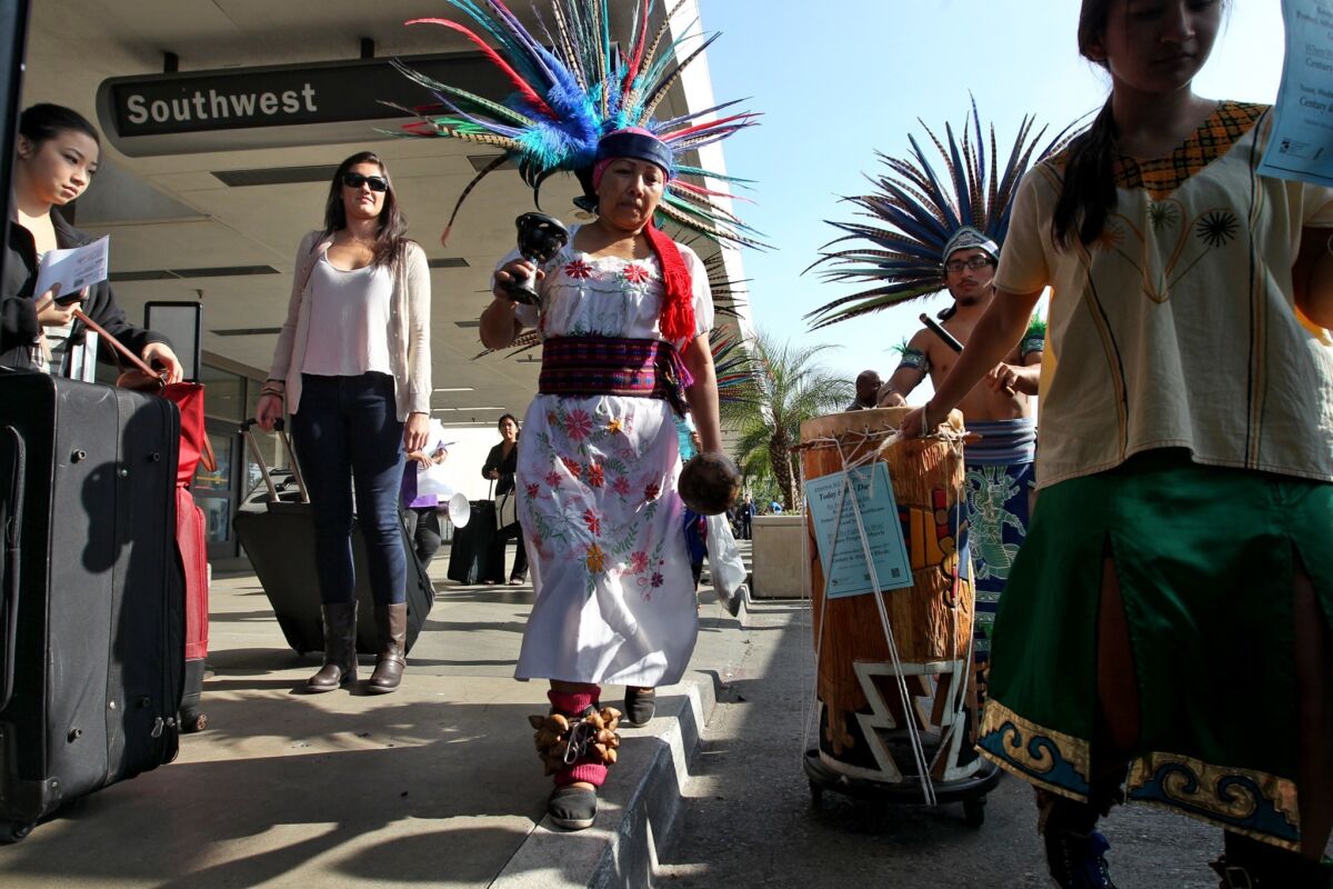 Holiday travelers Megan Kao and Courtney Poole, from left, watch as Cuauhtemoc Aztec dancers march through LAX to support workers last fall.