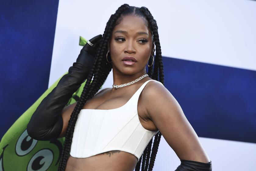 A woman with long, braided hair posing in a white crop top and silver necklace