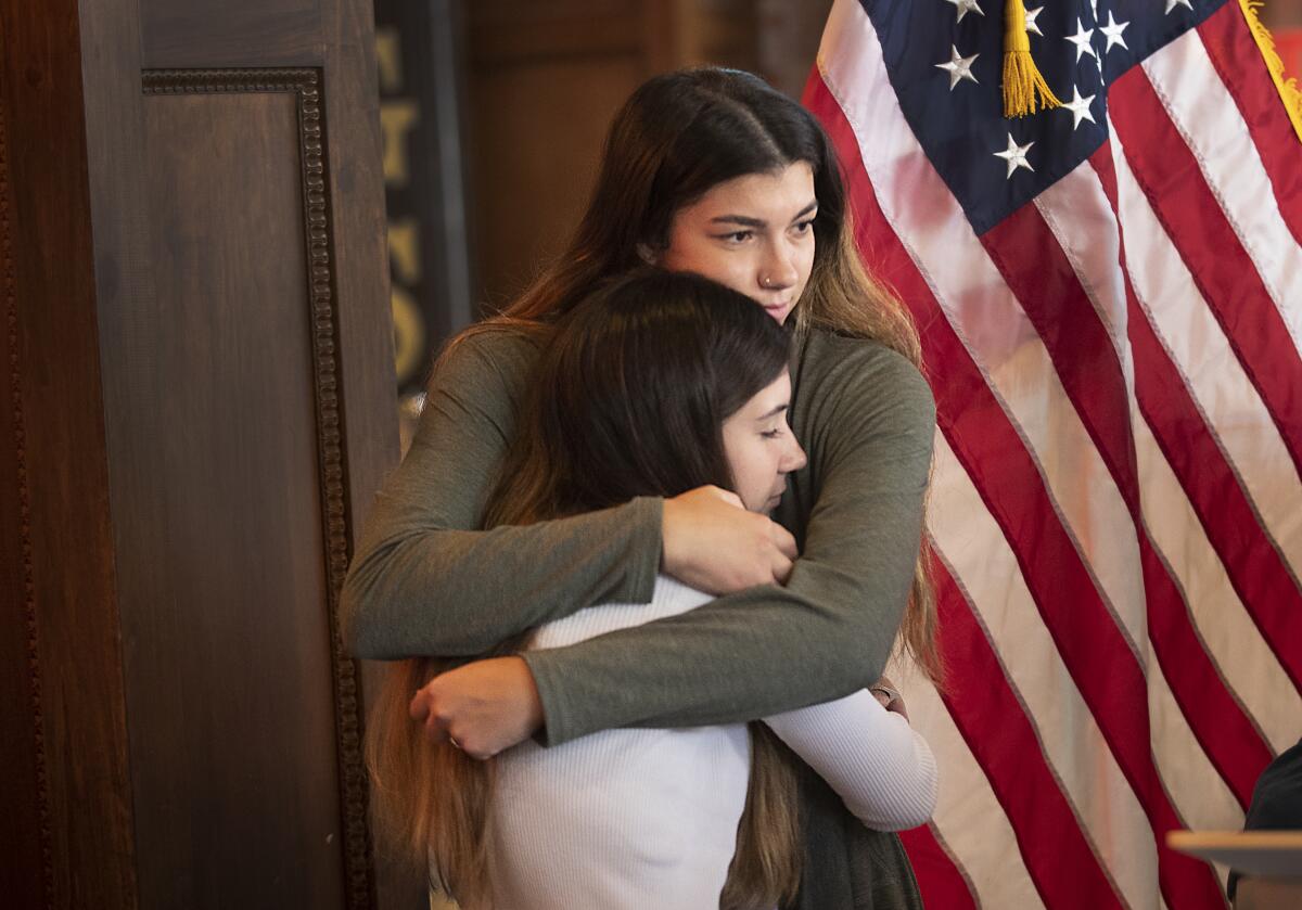 Two girls hug in front of an American flag