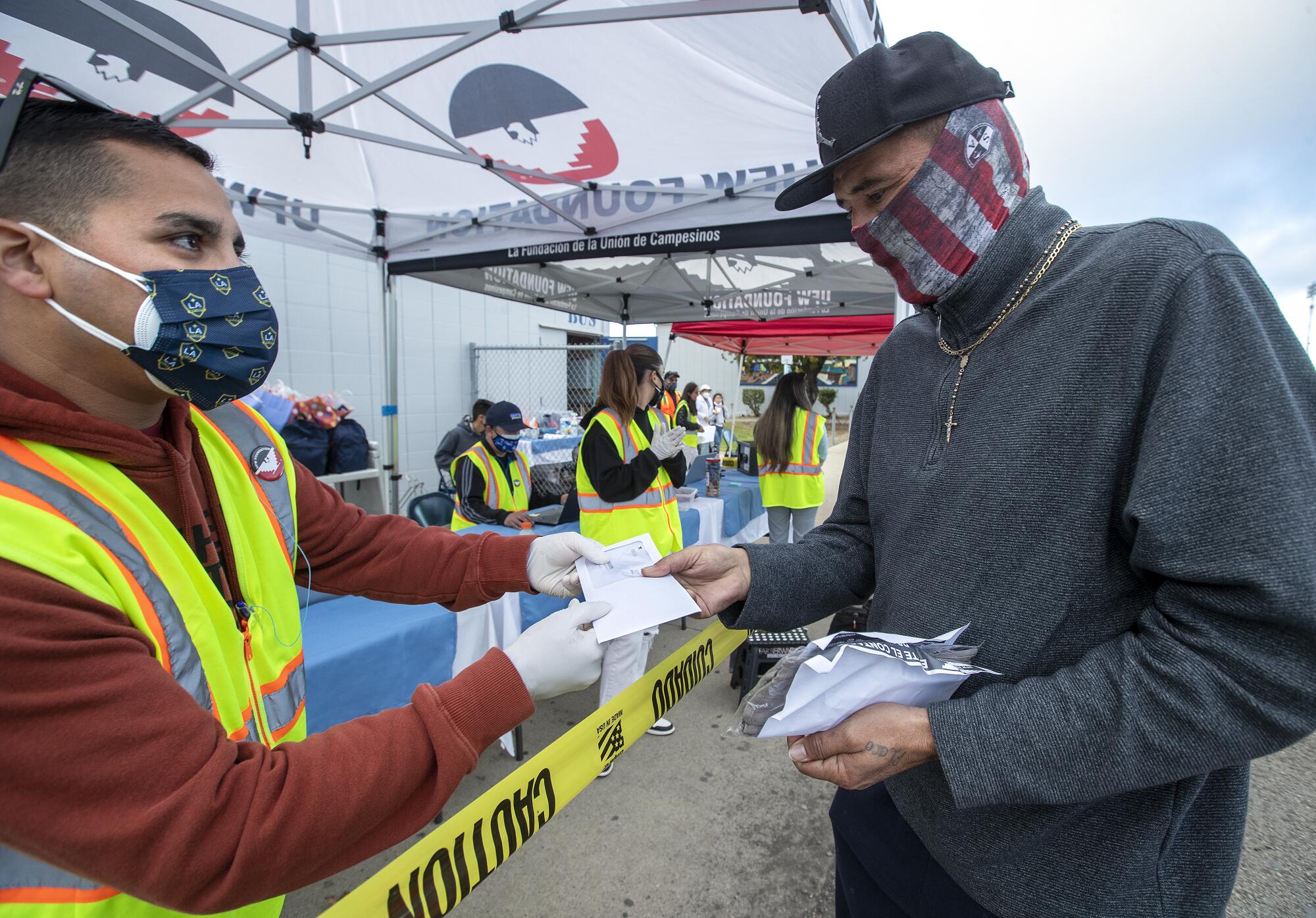 Volunteer Danny Garcia, left, gives an envelope containing a $100 prepaid card to farmworker Eduardo Garcia.