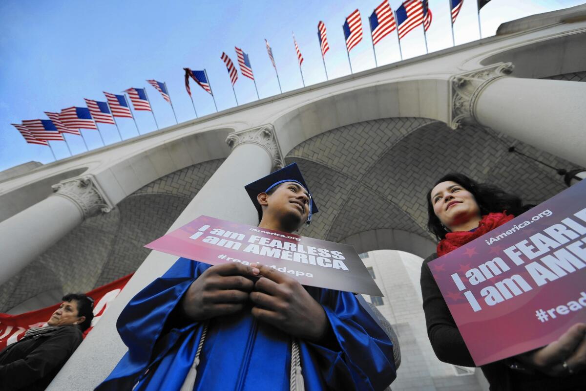 Jose Montes, 19, sporting his graduation cap and gown from Compton High School, and Paula Sarrad listen Tuesday at L.A. City Hall as speakers talk about expanded federal immigration programs.