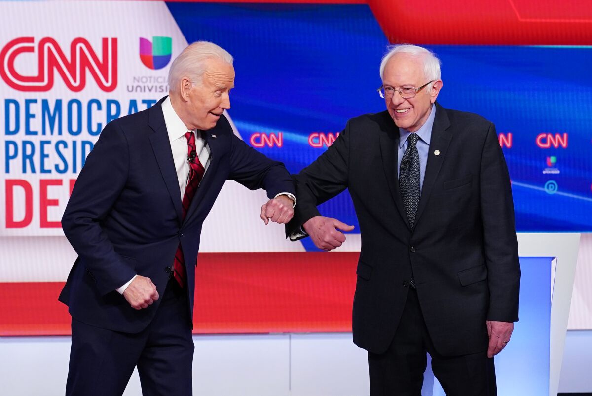 Joe Biden and Bernie Sanders greet each other with an elbow bump
