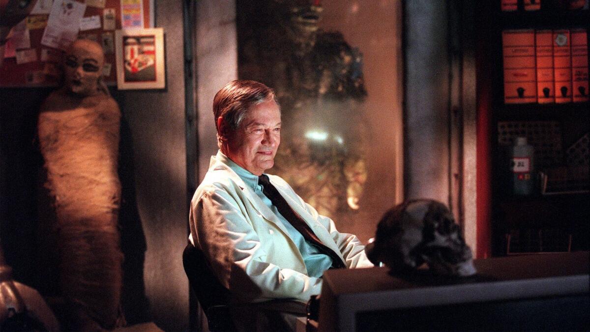 Roger Corman seated surrounded a skull and other horror movie props