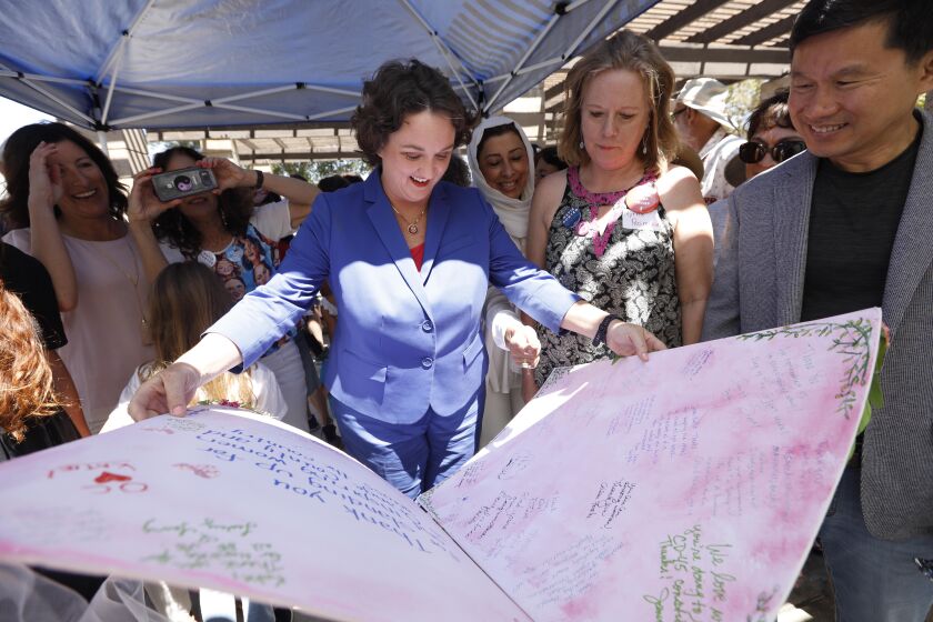 IRVINE, CA - AUGUST 24, 2019 - - Rep. Katie Porter, center, looks over a big card signed by supporters thanking her for her continued support of women while attending a rally at Northwood Community Park in Irvine on August 24, 2019. Porter spent the day criss-crossing her districts to make her case for re-election in a tough swing district. (Genaro Molina / Los Angeles Times)