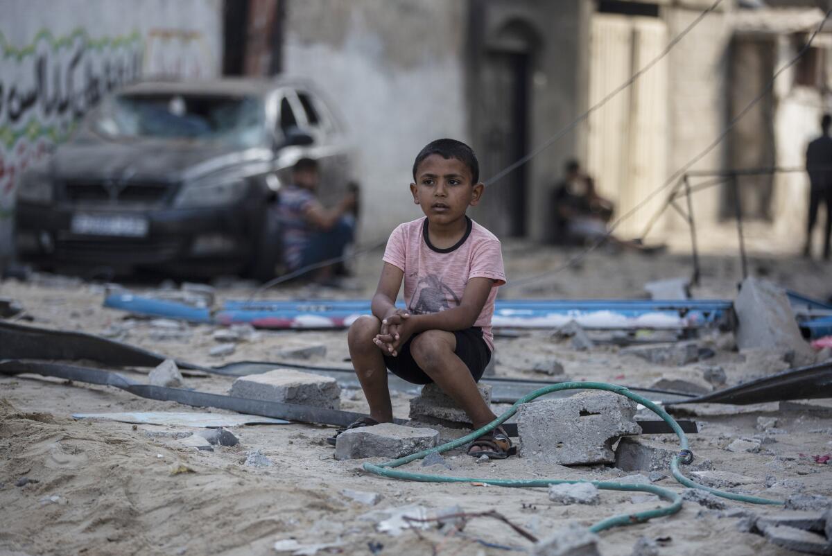 A boy sits amid debris near buildings