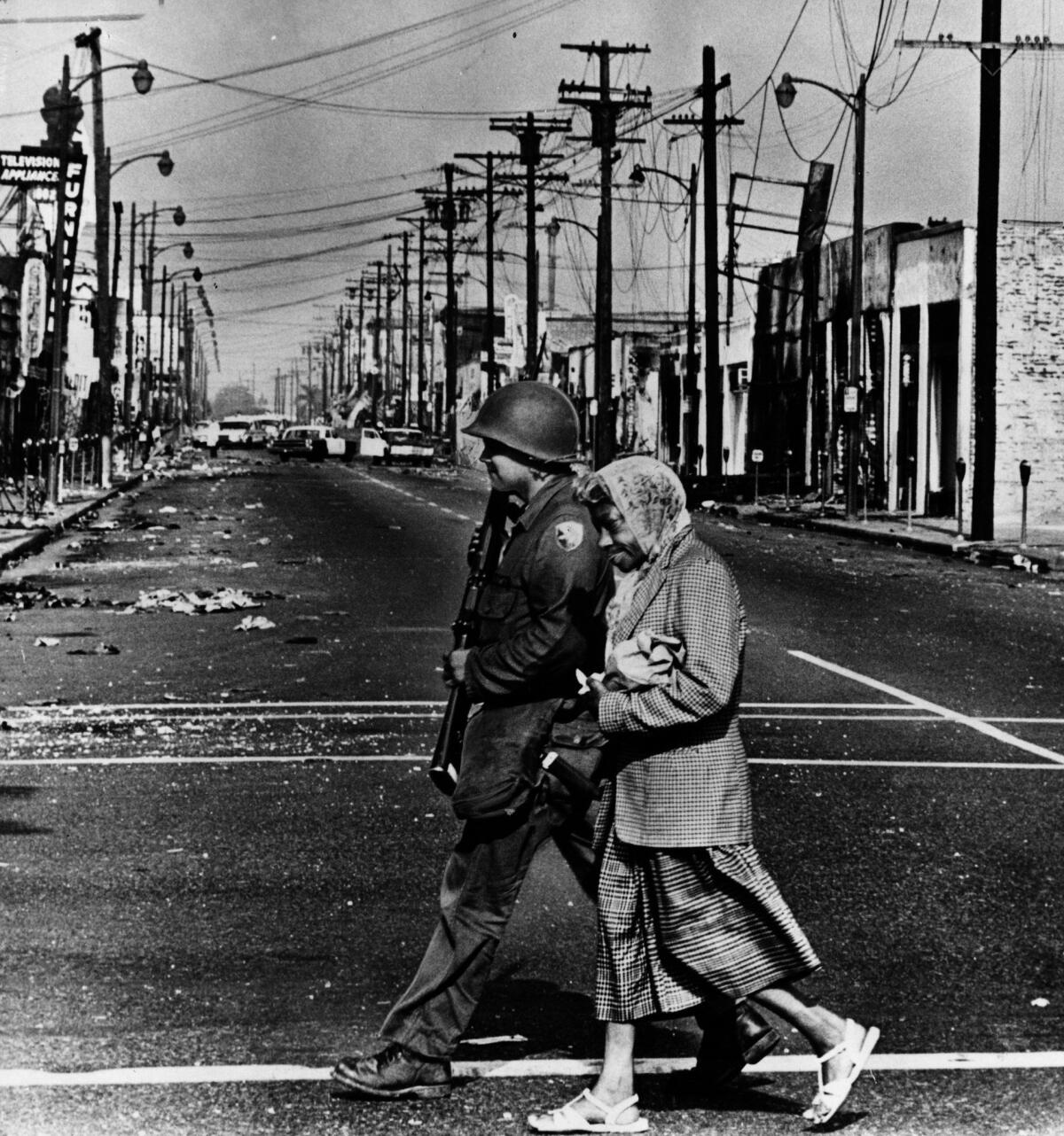 A National Guardsman escorts a Watts resident across rubble-strewn Wilmington Avenue after rioting in 1965.