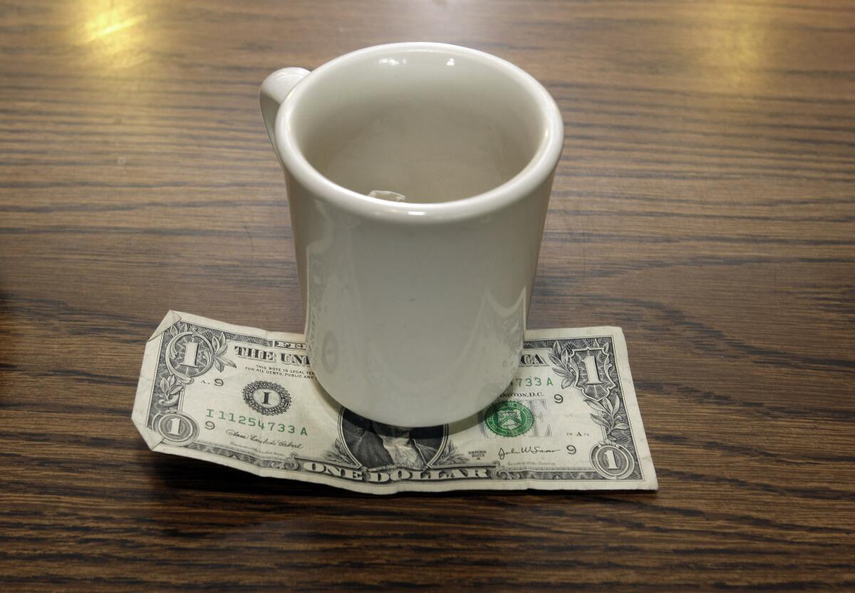 A dollar bill is under an empty coffee cup.