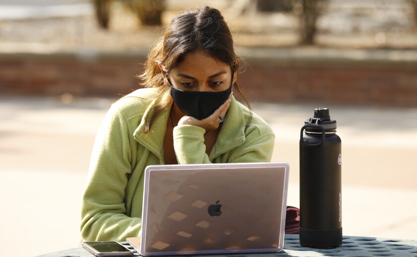 A female college student sits at an outside table looking at her computer.