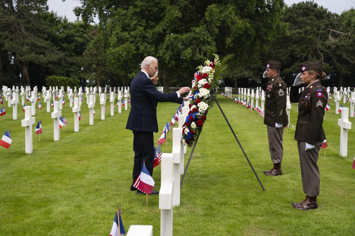 President Biden, Jill Biden laying a wreath in a field of white crosses near saluting military members