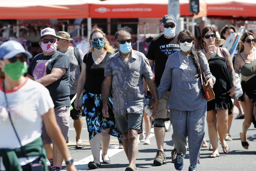 Beachgoers wear face masks to protect themselves as they walk in downtown Huntington Beach on Saturday.