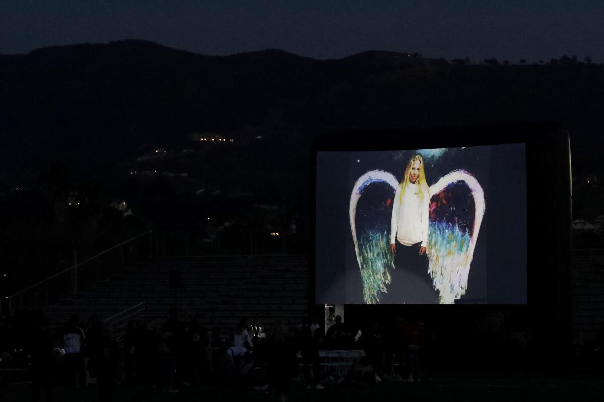 An image of Katie Meyer posing in front of a wings mural is projected at an outdoor memorial