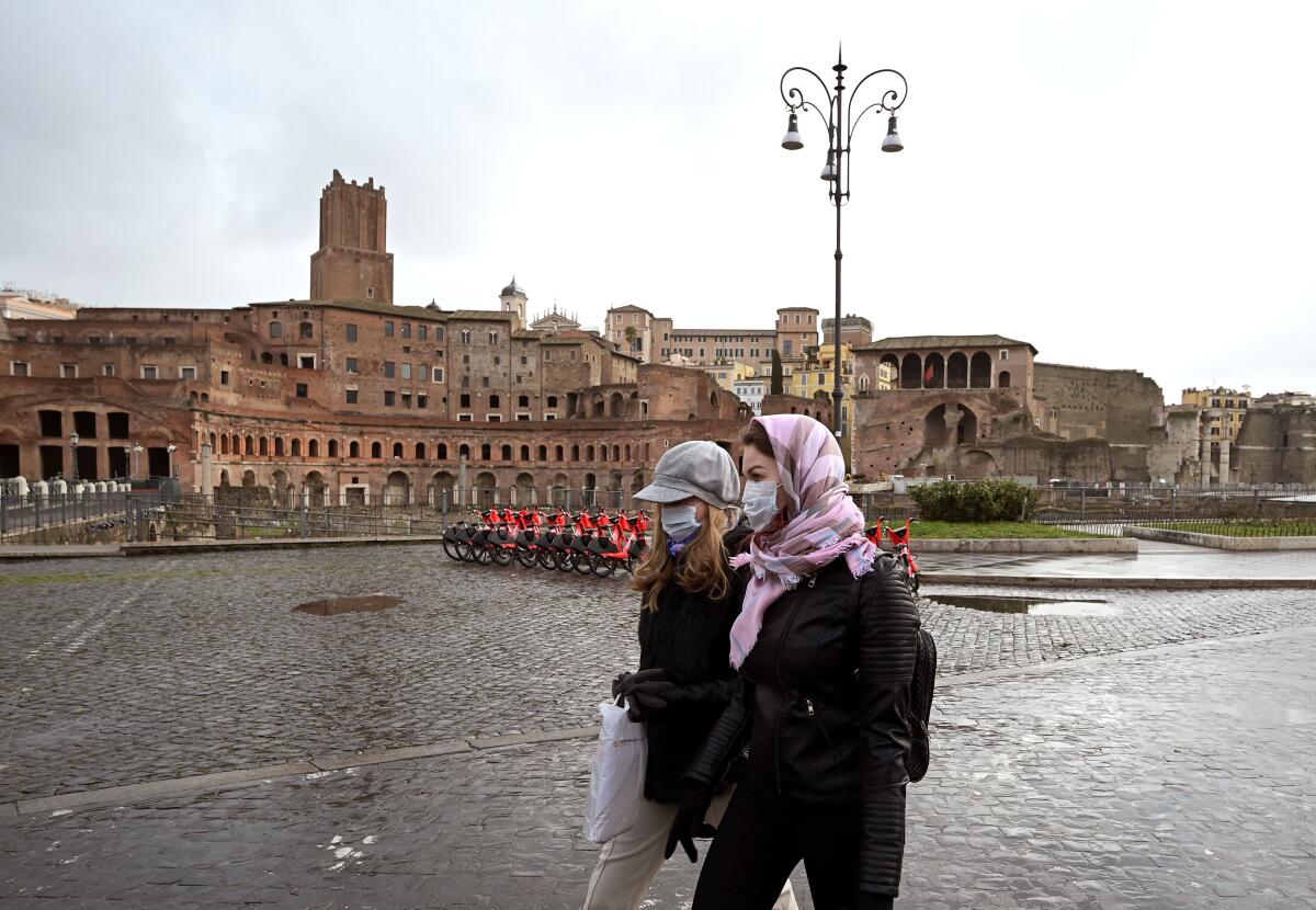 Two women wearing protective masks walks past the Trajan Forum in Rome on March 3, 2020.