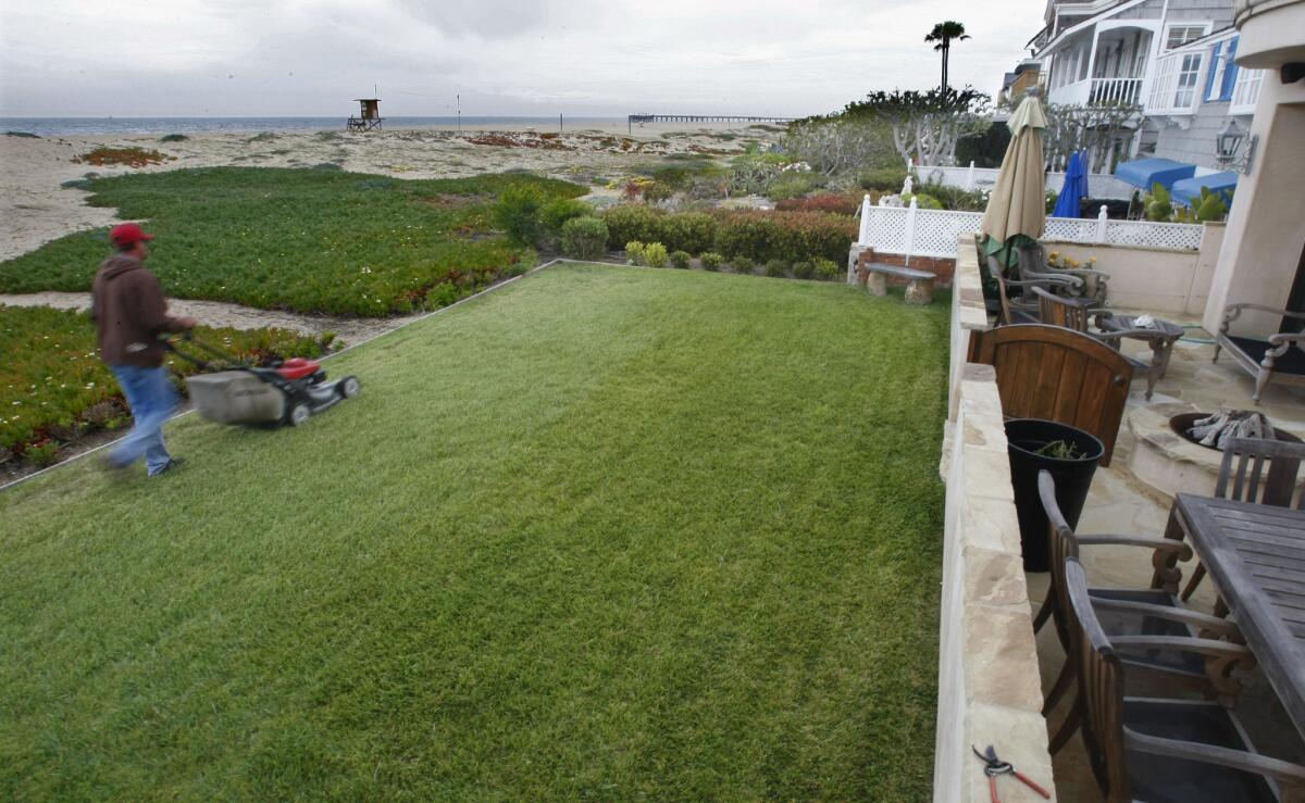 Landscaper Ron Rogers mows a lawn in 2012 on East Ocean Front on the Balboa Peninsula. Technically the homeowner's property ends at the wall to the right and the grass is on the public land. A new law allows the California Coastal Commission to fine those who block public access to the beach.