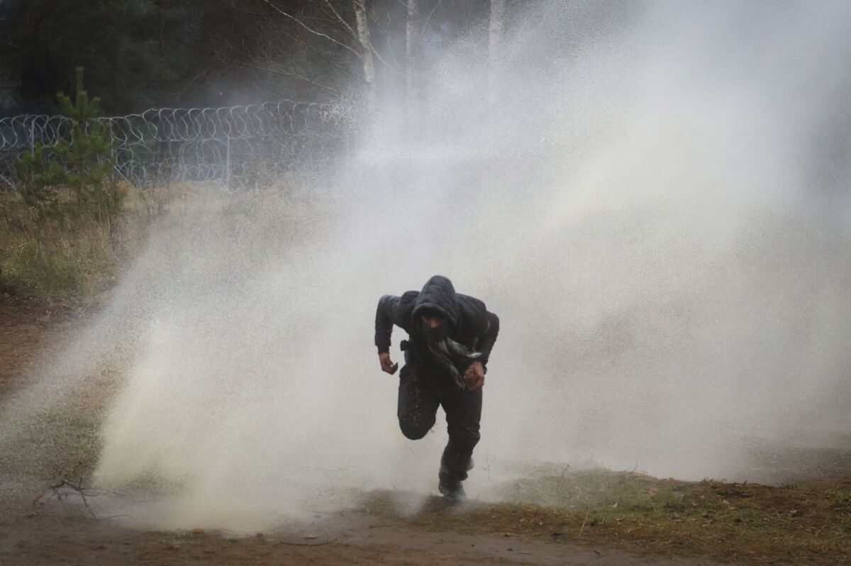 A man runs away from a water cannon during clashes between migrants and Polish border guards at the Belarus-Poland border near Grodno, Belarus, on Tuesday, Nov. 16, 2021. Polish border forces say they were attacked with stones by migrants at the border with Belarus and responded with a water cannon. The Border Guard agency posted video on Twitter showing the water cannon being directed across the border at a group of migrants in a makeshift camp. (Leonid Shcheglov/BelTA via AP)