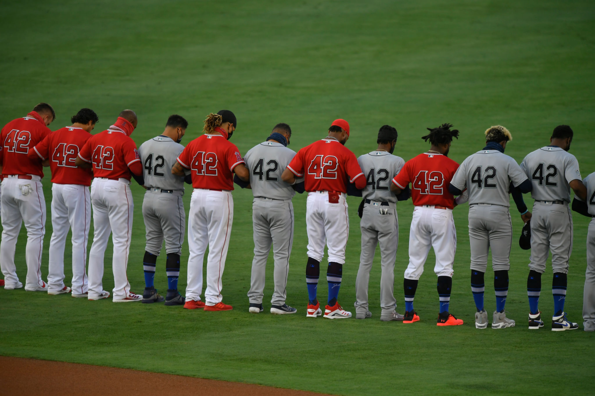 Players on the Angels and Seattle Mariners lock arms on the field during the national anthem.