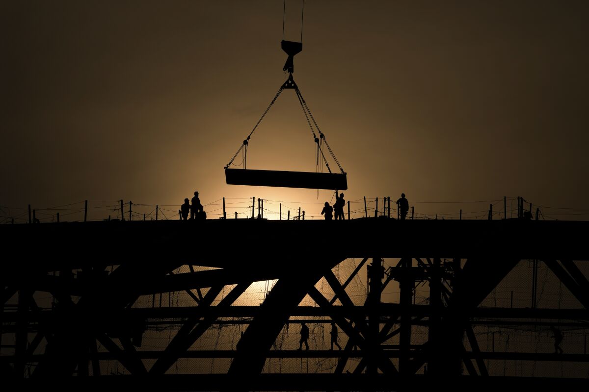 FILE - Workers are silhouetted against a sunset as they handle a steel frame on the roof of the Workers' Stadium under construction in Beijing, China, Monday, Feb. 28, 2022. China, the world’s top emitter of carbon dioxide and other greenhouse gases that cause global warming, has seen a notable dip in its carbon emissions over the past three quarters, as of June 1, 2022 — but it’s not clear how long the drop will continue. (AP Photo/Andy Wong, File)