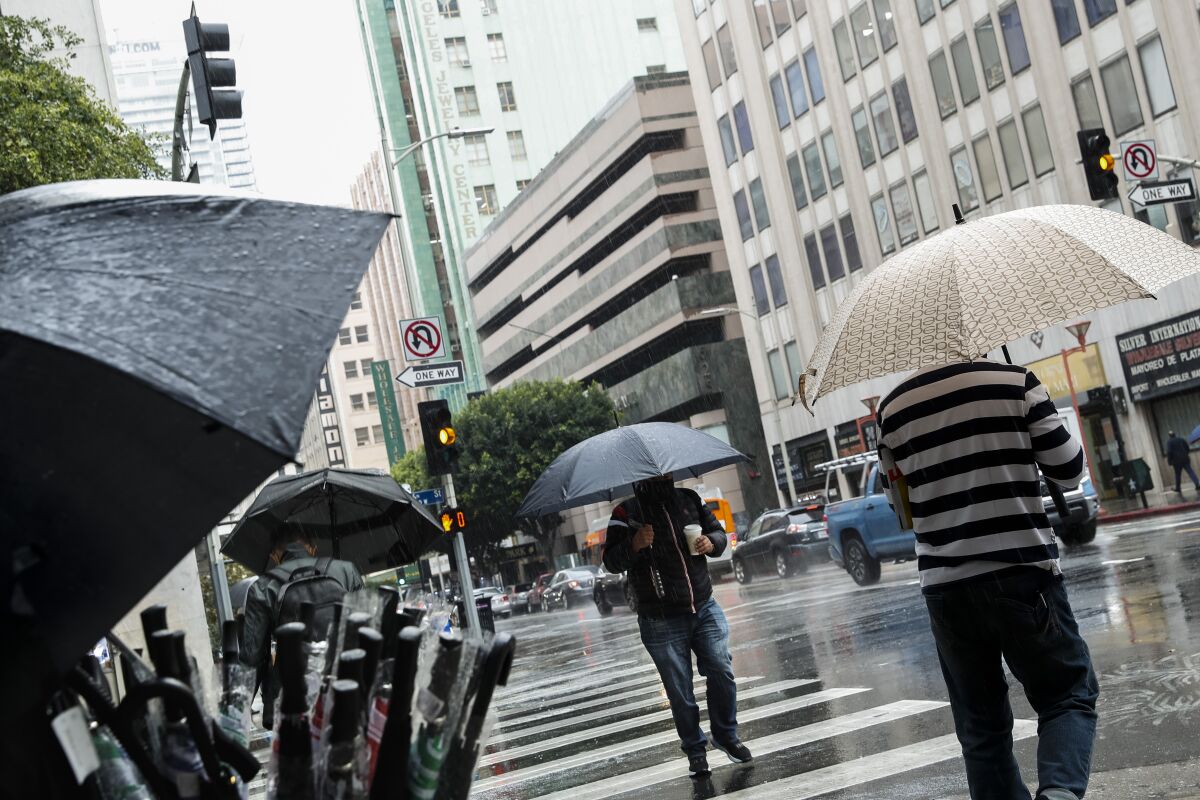 A vendor sells umbrellas while pedestrians with umbrellas walk along a city street in the rain