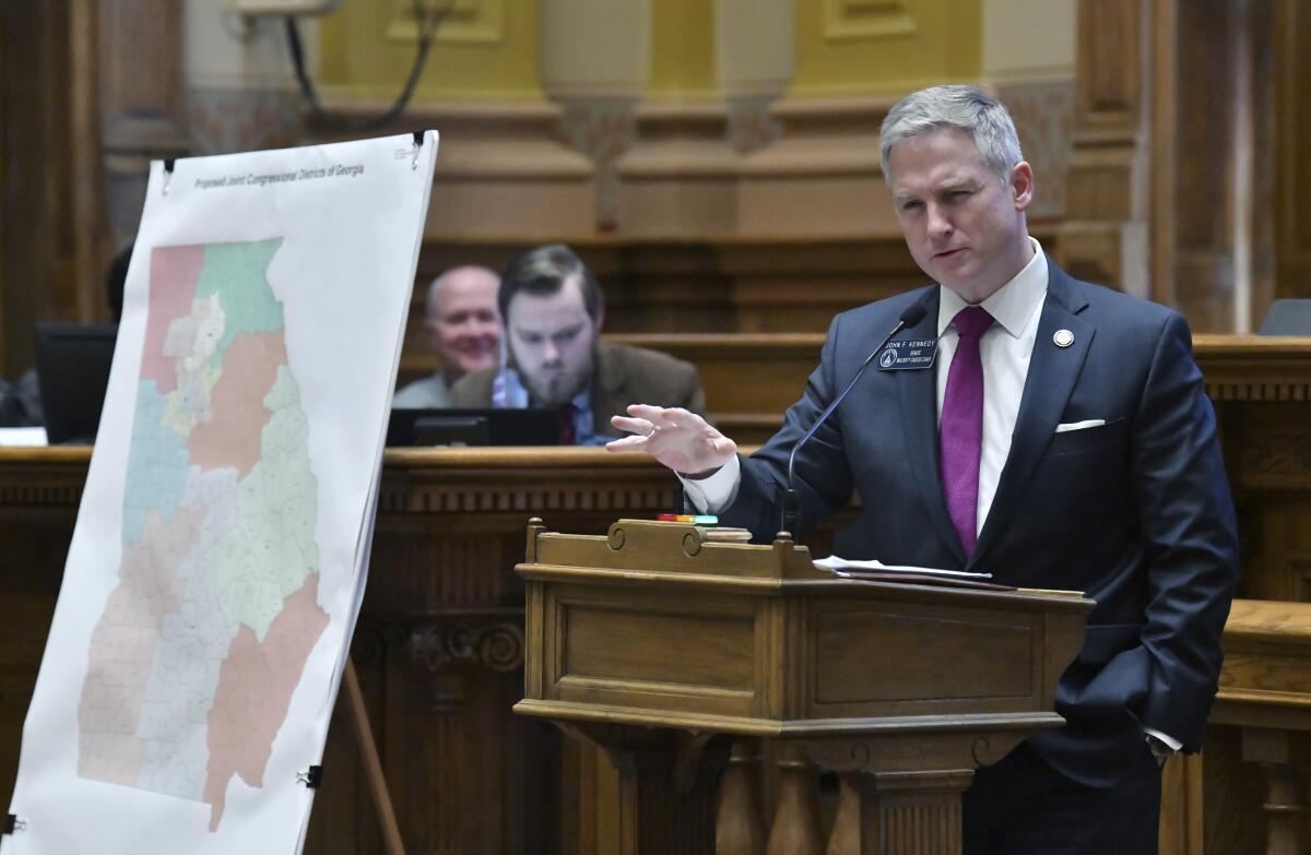 A man in a suit stands next to congressional maps