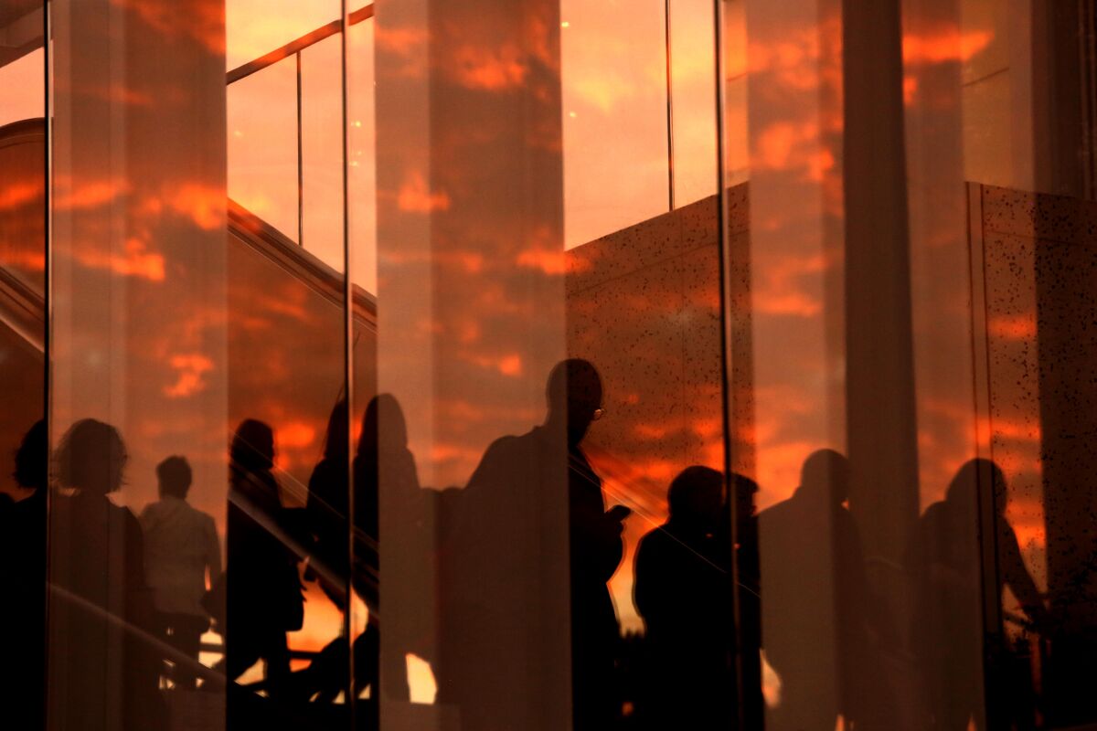 Silhouettes of people are reflected on a glass along with a red sunset sky. 