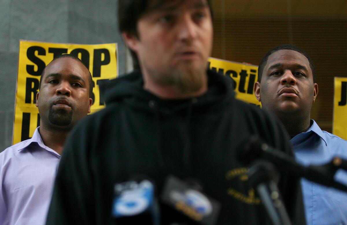 Perry Grays, right, and his father-in-law, Adrian Brown listen as Mike Woods, a neighbor and witness to Grays' beating, speaks during a press conference outside the Long Beach Police Department in March 2011.