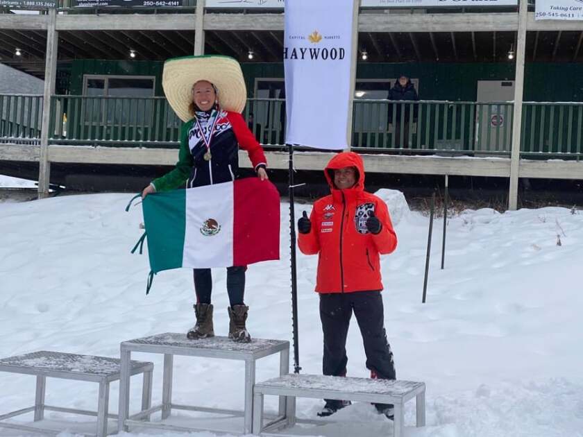 Karla Schleske stands on a podium holding up the Mexican flag after winning a ski competition