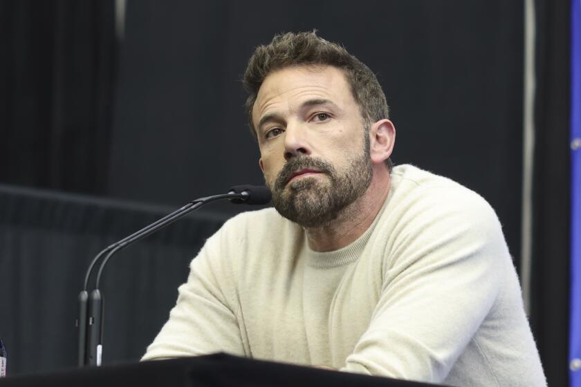 Ben Affleck in a white long sleeve shirt sitting in front of a microphone
