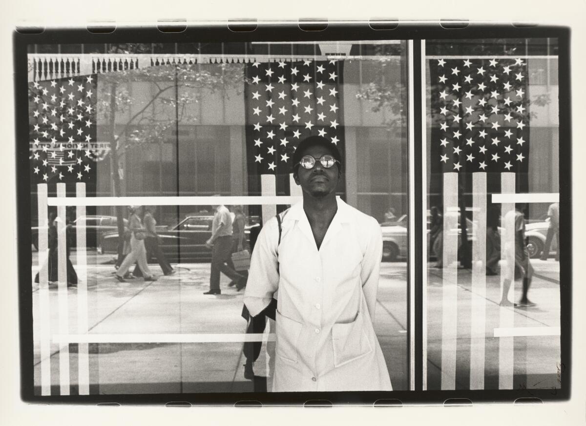 A portrait of a man standing in front of a window and three American flags