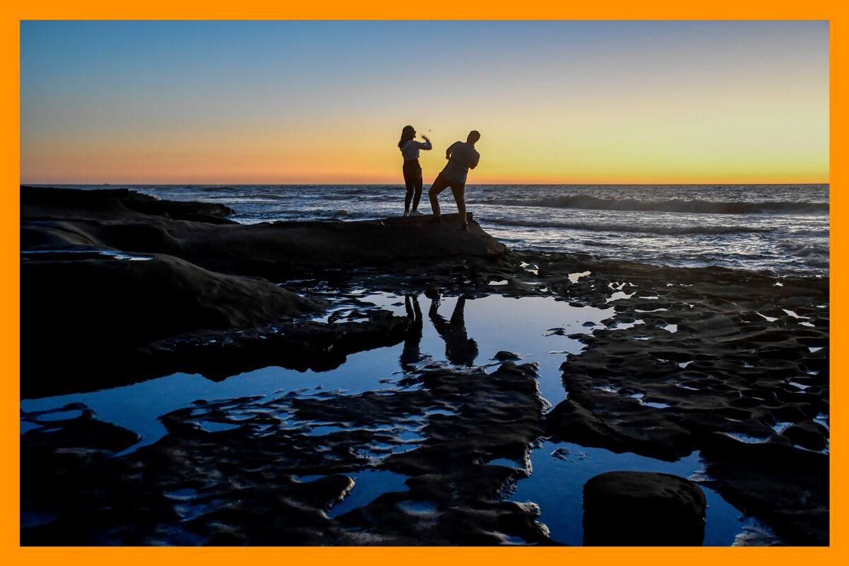 Two people visiting a tide pool are silhouetted against the setting sun.