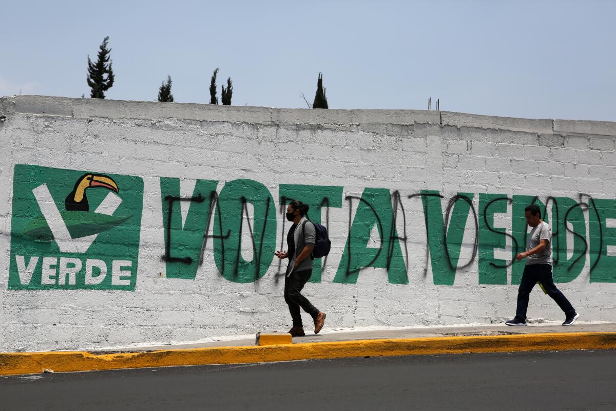 Archivo - Peatones caminan cerca de un mural con una consigna de "vota verde" 