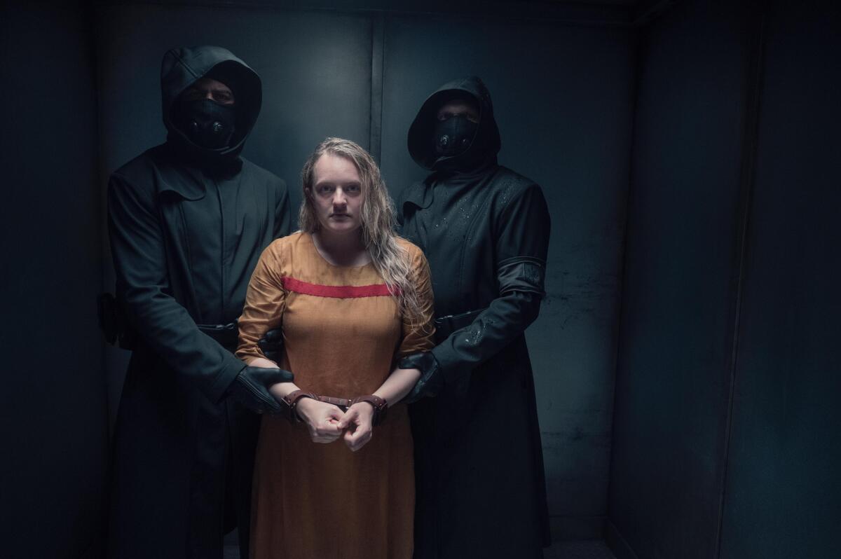 A woman prisoner being led by two masked, hooded figures in black.
