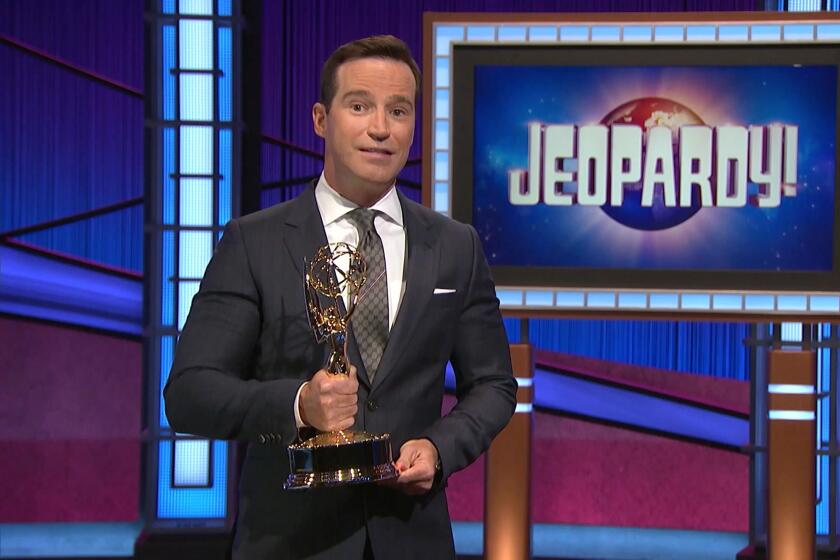 A man in a suit holding a golden trophy on the 'Jeopardy!' set