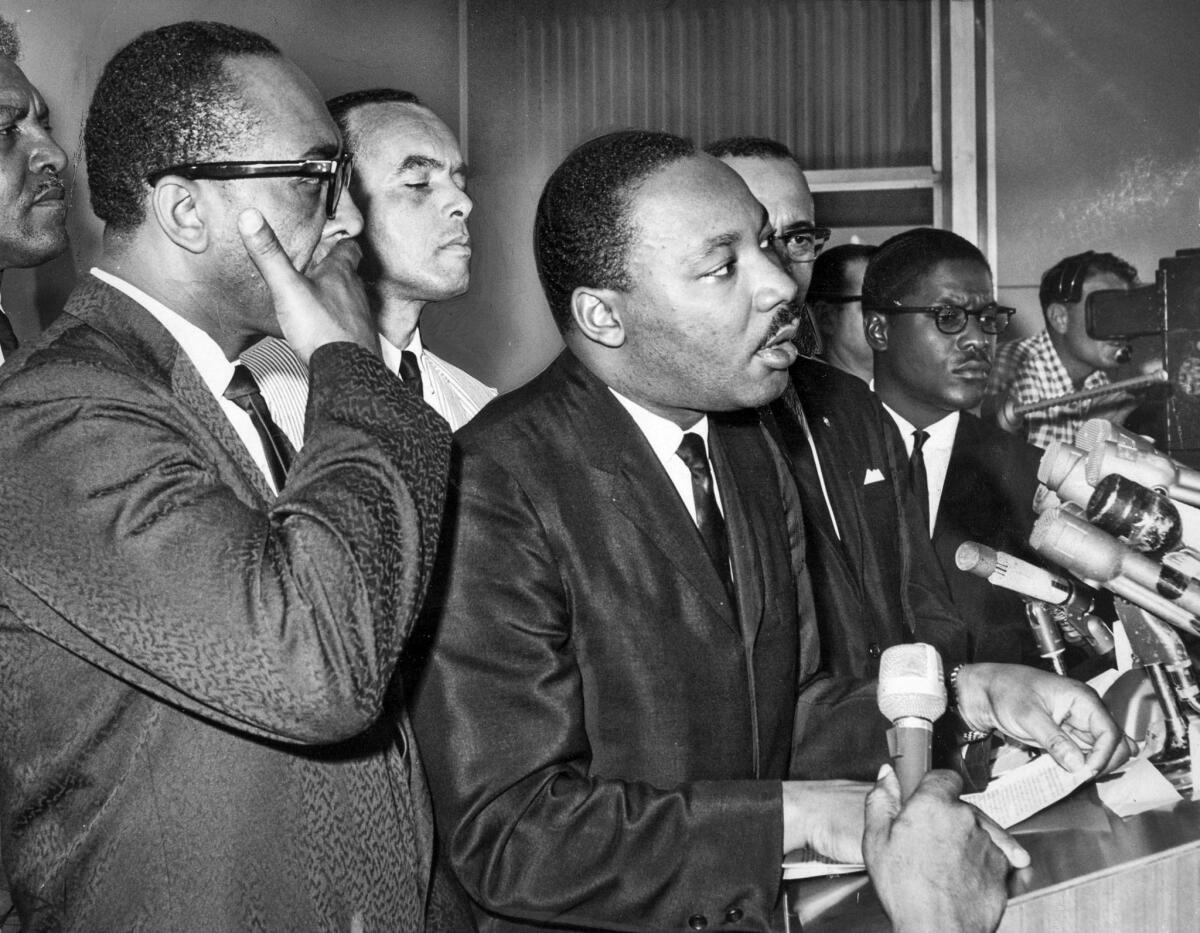 Aug. 17, 1965: King speaks to the press after arriving at LAX on a trip to try to calm racial tensions in the city following the Watts riots. Behind him are the Rev. H. H. Brookins, left, and Norman B. Houston.