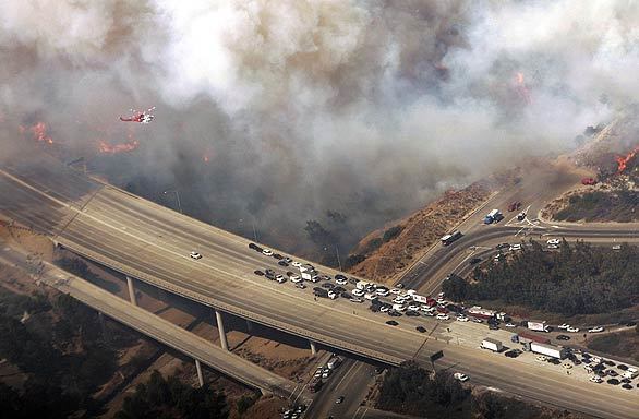 Cars travel in the wrong direction on the 118 Freeway as they are directed back to an onramp, where they exited to get out of the way of smoke and flames from the fire burning in Porter Ranch.