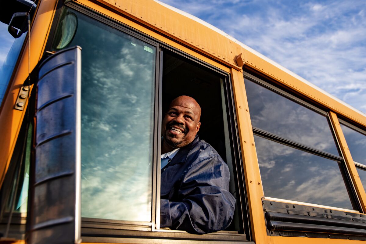 A driver smiles from the window of a school bus.
